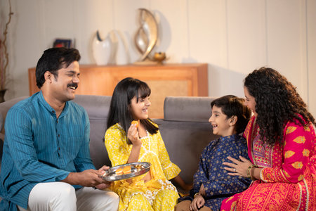 Indian family sitting on sofa in living room and eating food at homeの写真素材