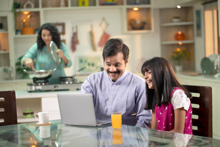 happy indian family using laptop computer and drinking orange juice at homeの写真素材