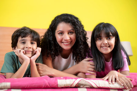 Portrait of happy mother and her children lying on bed at homeの写真素材