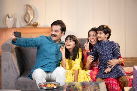 indian family taking selfie with mobile phone in living room at homeの写真素材
