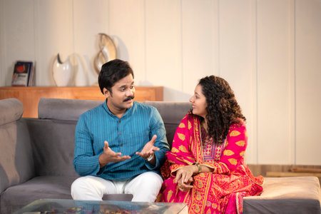 Indian young couple sitting on sofa at home, talking and smiling.