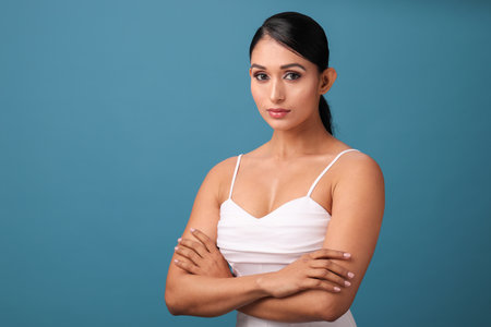 Portrait of beautiful young woman with crossed arms against blue background.の写真素材