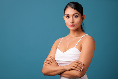 Portrait of a beautiful young woman with arms crossed against blue backgroundの写真素材