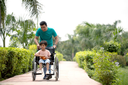 Happy asian man pushing wheelchair with his son in the park.の写真素材