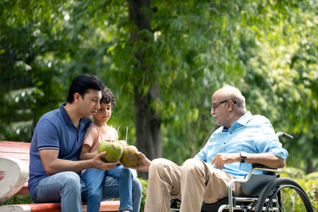 Senior man in wheelchair and his grandson drinking coconut juice in the parkの写真素材