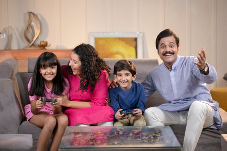 Happy family playing video games together at home sitting on a sofaの写真素材