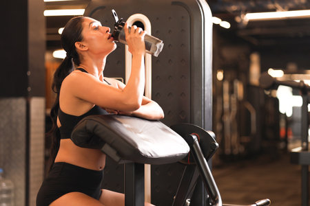 Sporty young woman drinking water from a bottle while working out at the gymの写真素材