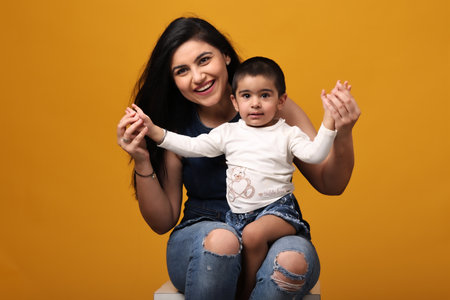 Portrait of a happy mother and her little daughter isolated over yellow backgroundの写真素材