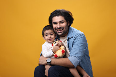 Indian father with his little son on yellow background. Happy family concept