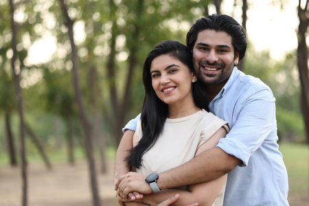 Indian couple in love embracing and smiling at camera in the park.