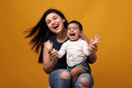 Portrait of a happy mother with her son isolated over yellow backgroundの写真素材