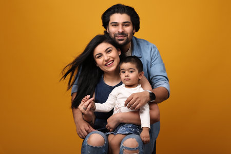 happy indian family with little daughter sitting on yellow background, studio shot