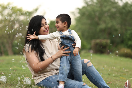 Mother and son playing with soap bubbles in the park, outdoor shoot