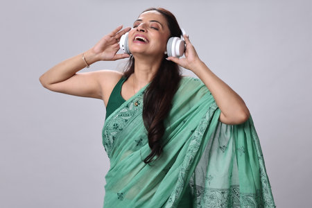 Young Indian woman listening to music with headphones. Isolated on grey backgroundの写真素材