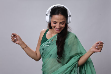 Young Indian woman listening to music with headphones on a grey background.の写真素材