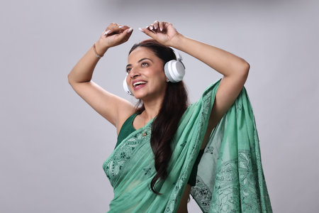 Beautiful young Indian woman listening to music with headphones on grey background