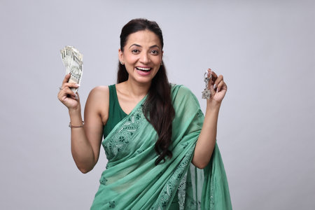 Young Indian woman holding money and winning lottery ticket on grey background.の写真素材
