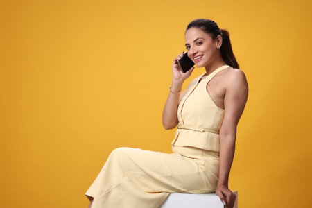 Beautiful young woman talking on mobile phone against yellow background. Space for textの写真素材