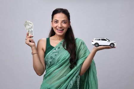 Indian woman holding dollar banknotes and car model on gray background.の写真素材
