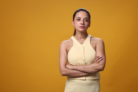 Portrait of a confident businesswoman standing with arms crossed against yellow backgroundの写真素材