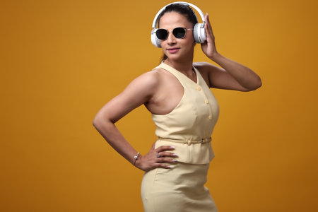 Beautiful asian woman listening to music with headphones over yellow backgroundの写真素材