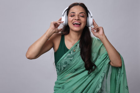 Indian woman in saree listening to music with headphones on grey backgroundの写真素材