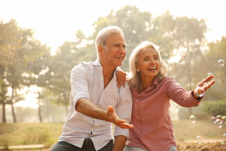 Happy senior couple playing with soap bubbles in the park. Retirement concept