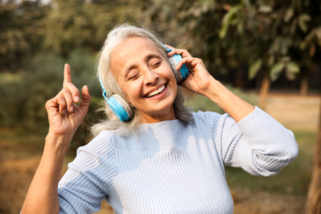 Happy senior woman listening to music in the park. Mature woman with headphones and dancing.