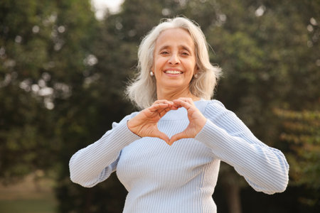 Portrait of smiling senior woman making heart shape with hands in park