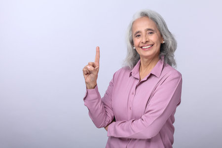 Portrait of happy senior businesswoman pointing finger up against gray backgroundの写真素材