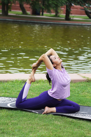 Young woman practicing yoga in the park, sitting on a mat.