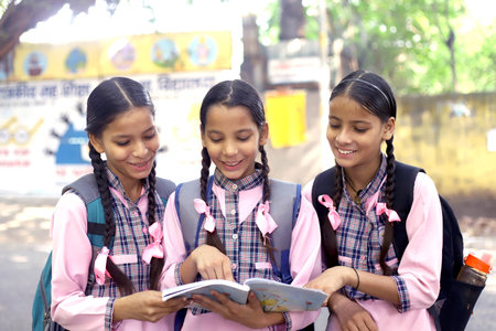 Three girls in school uniform reading a book and smiling at the cameraの写真素材
