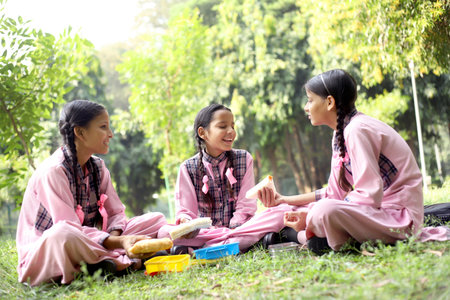 Three girls in pink uniforms eating and talking in the parkの写真素材