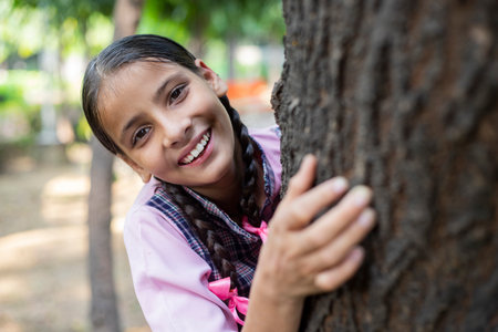Portrait of smiling schoolgirl leaning against tree trunk in school yardの写真素材