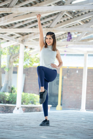 Full length portrait of a smiling young woman doing stretching exercise in the city