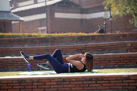 Young beautiful woman doing abs exercises in the city park. Fitness concept.