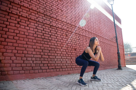 Portrait of a beautiful young brunette woman in sportswear posing against the background of a red...