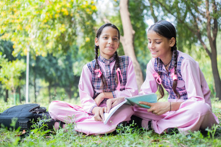 Two little girls reading a book together in the park. Education concept.の写真素材