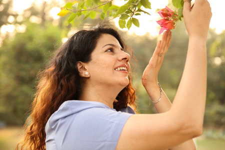 Portrait of beautiful mature woman with flower in park on summer day