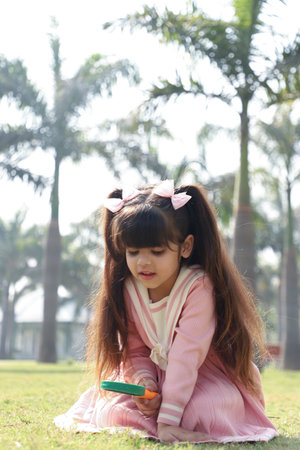 Little girl sitting on the grass in the park and playing with a wooden stickの写真素材