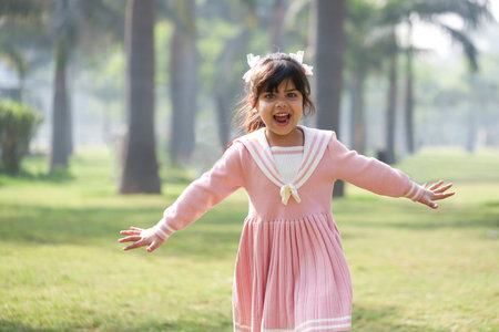 happy asian little girl in pink dress jumping in the park.の写真素材