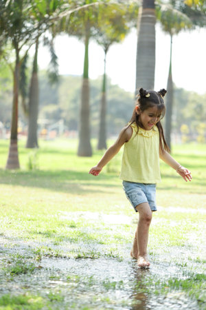 Little girl playing in a puddle in the park on summer dayの写真素材