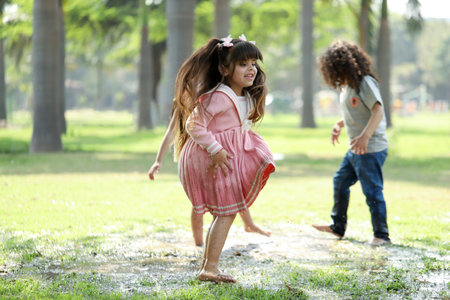 Cute little girl running in the park with her father in the backgroundの写真素材
