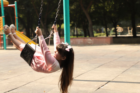 Little asian girl swinging on swing in the playground at park.の写真素材