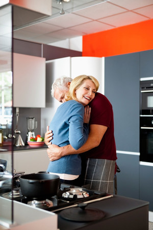 Senior Couple Hugging in Kitchenの写真素材