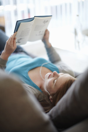 A girl lying on the sofa reading a bookの写真素材