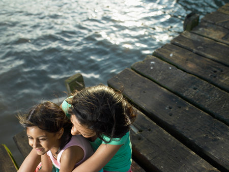 Mother and daughter sitting on dockの写真素材