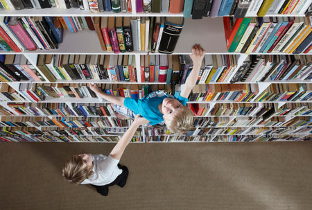 Girl helping boy climb bookshelvesの写真素材