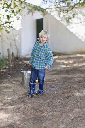 Boy carrying heavy pail outdoorsの写真素材