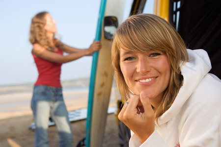 Woman at the beach smiling with other woman in background holding surfboard.の写真素材